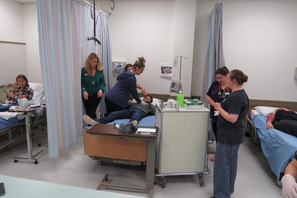 An image of females in scrubs attending to an individual lying on a hospital bed.