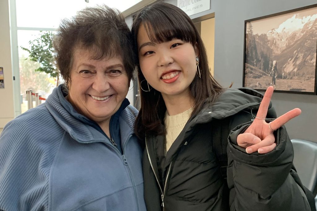 An image of a female homestay host and female international student waving at the camera and smiling. 