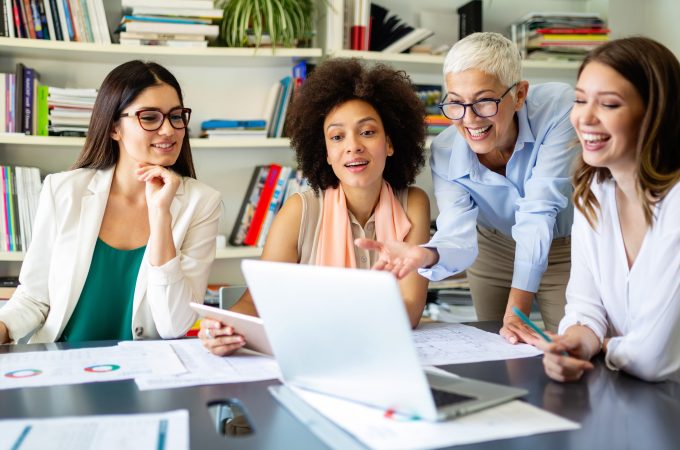 Four business women looking at a laptop computer.