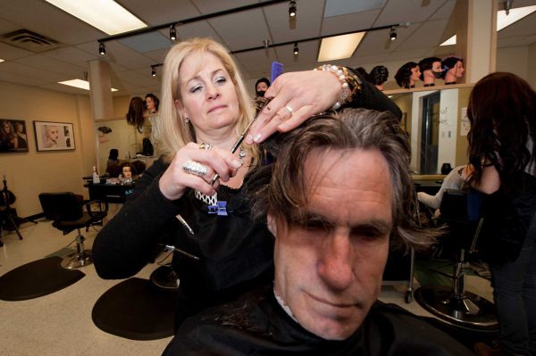 Image of blond woman cutting hair of man.