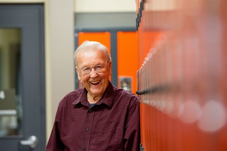 Image of elderly man smiling as he leans against orange lockers.
