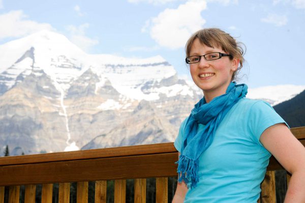 Image of woman in glasses standing on balcony overlooking a mountain range.