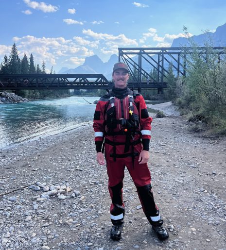 Image shows man in a wet suit and gear standing next to a river.