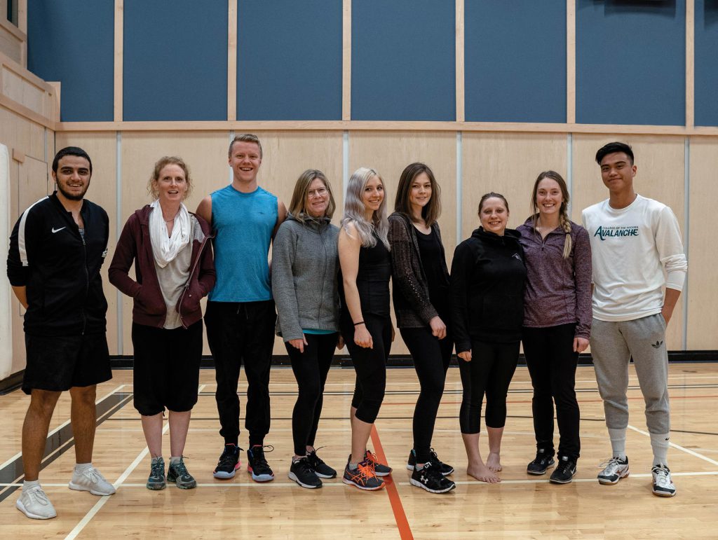 Image of eight students with their instructor Jani Vogell, posed together and looking at the camera in College of the Rockies' gym.