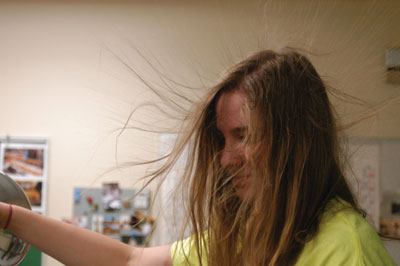 Image of math competition participant demonstrating the Van de Graaff electrostatic generator, with her hair standing up wildly.