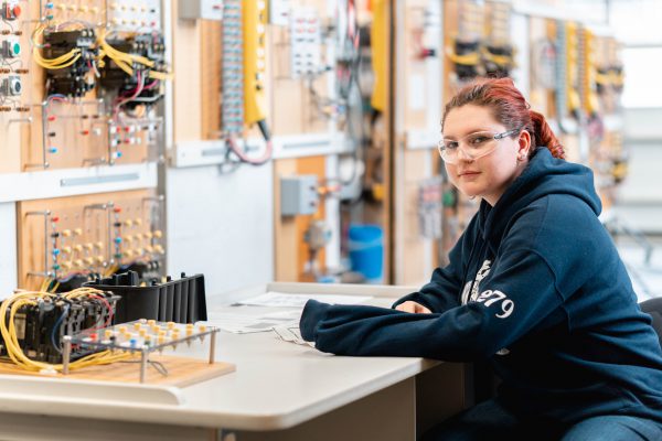 Image of young woman in safety glasses sitting in front of electrical boards