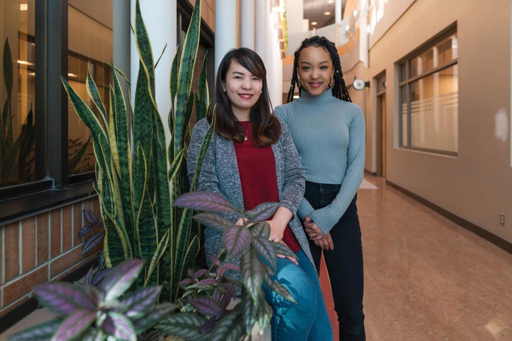 Image shows two young women standing in a hallway.