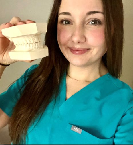Image shows woman in scrubs holding impressions of teeth, smiling at the camera