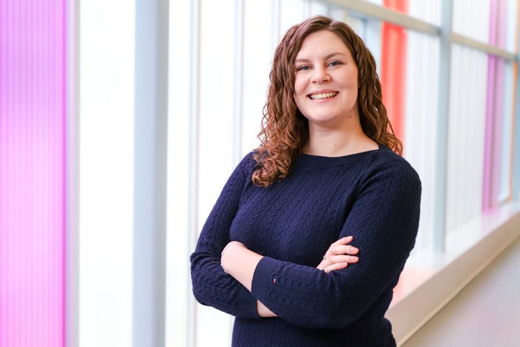 Image shows woman with arms casually crossed, smiling at the camera