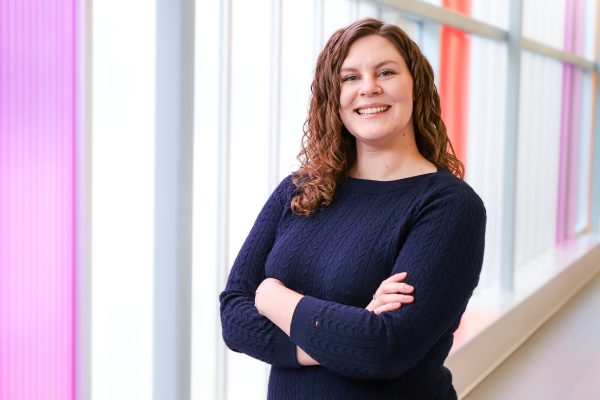 Image shows woman with arms casually crossed, smiling at the camera