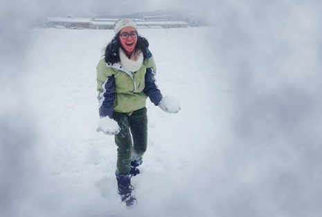 Image of woman in glasses and dark hair playing in snow with large smile on her face.