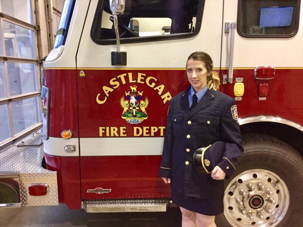Image of young woman in firefigther gear, standing next to a Castlegar Fire Dept. truck.