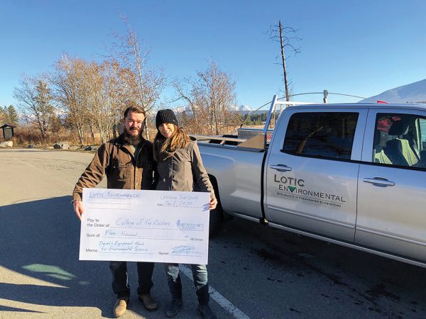 Mike and Corinna Robinson from Lotic Environmental hold a large cheque while standing in front of their company truck.