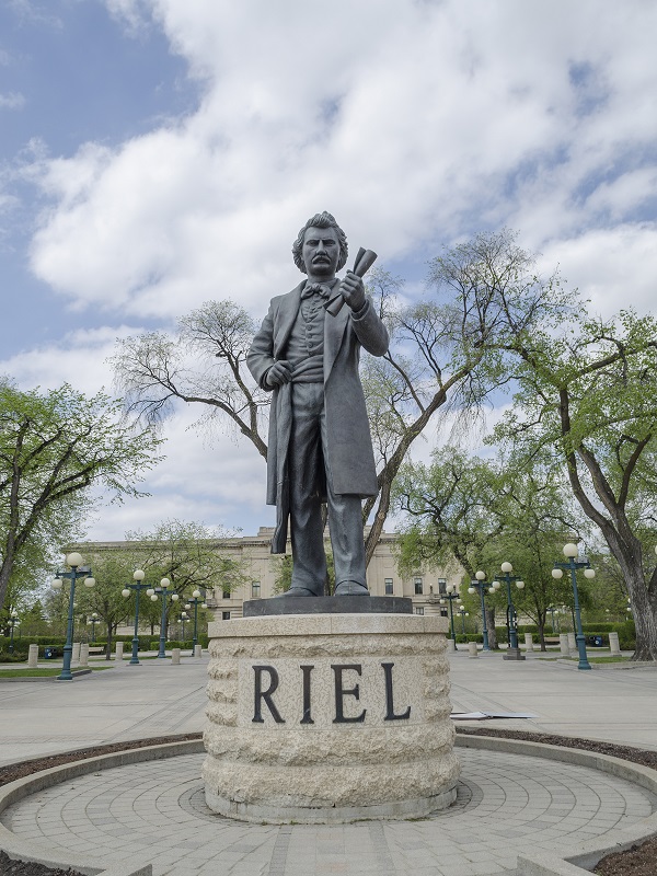 Image shows a statue of Louis Riel at the Manitoba Legislative Grounds.