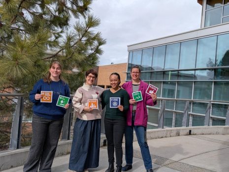Image shows four women standing outside College of the Rockies, holding cards depicting 6 of the UN's Sustainable Development Goals.