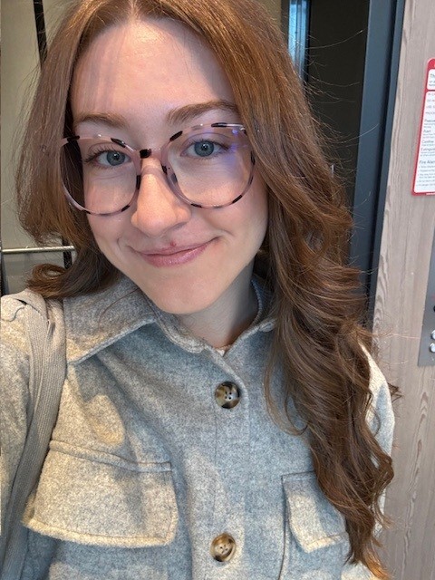 Image shows woman with long hair and glasses smiling at the camera.