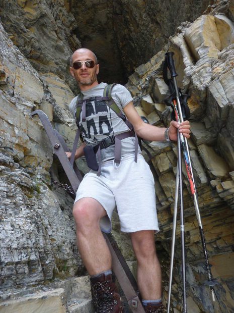 Image of man in sunglasses with backpack on rocky ledge.
