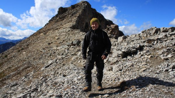 Image shows man in a parka and touque high up on top of a mountain