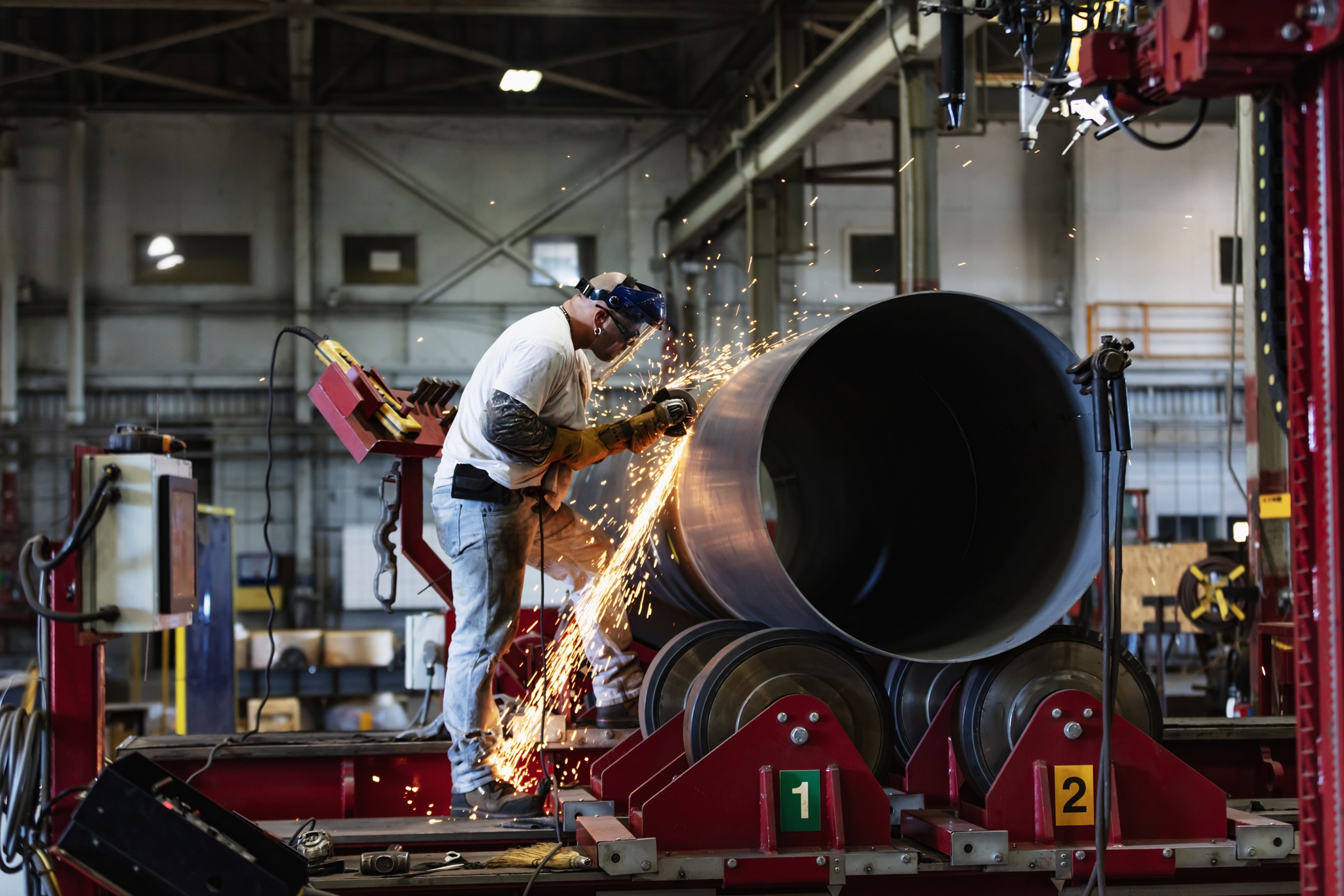 A mid adult man working in a metal fabrication plant on a large steel cylinder. Sparks are flying as he grinds down the welds.