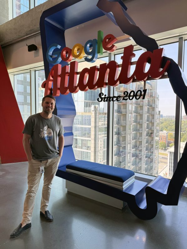 Image shows man standing with his hands in his pockets next to a Google Atlanta sign