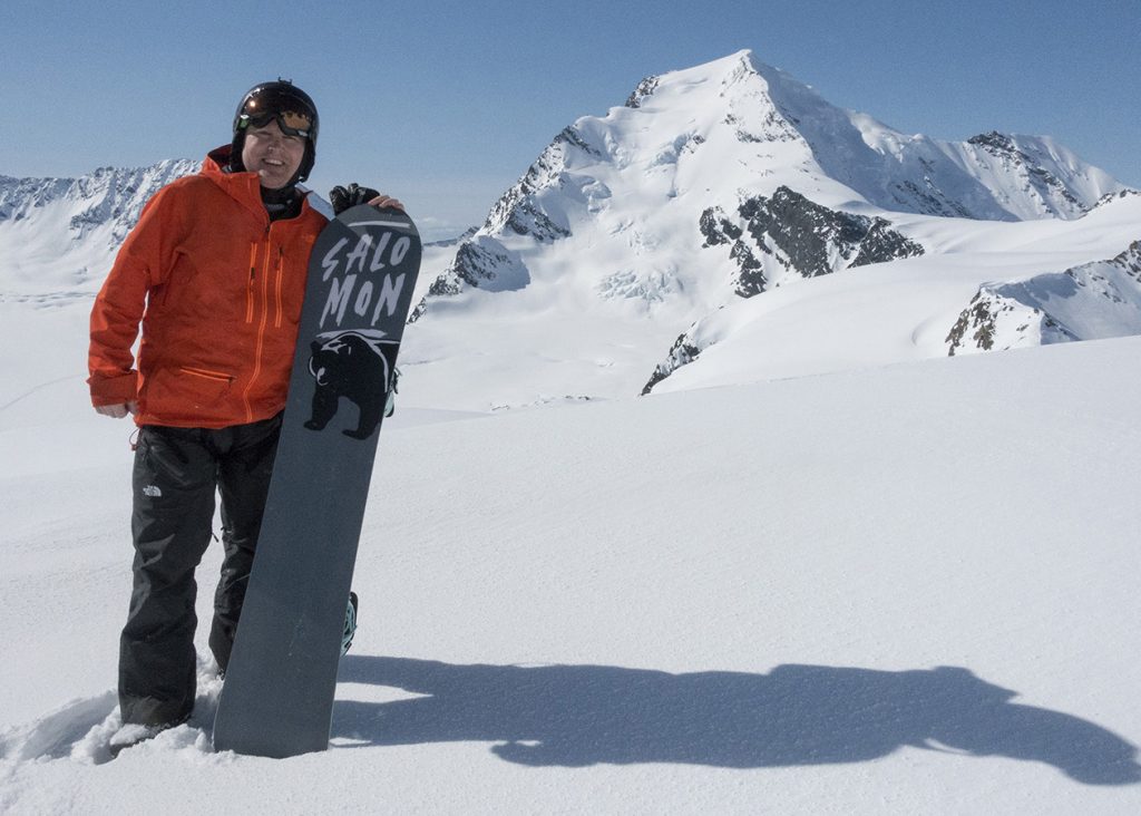 Man standing with snowboard on mountain.