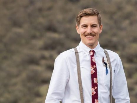 Image shows mustached man in white button-up shirt, suspenders and tie