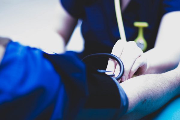 An image of an arm with a blood pressure cuff on it with another hand holding a stethoscope to the inside of the arm.