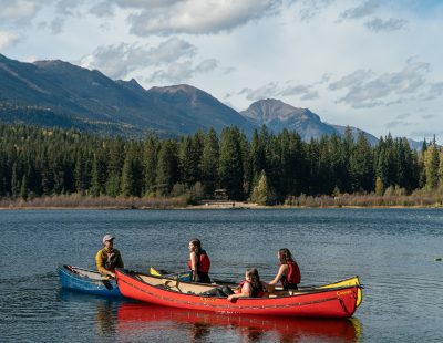 Image shows four people in two canoes on a lake surrounded by mountains.