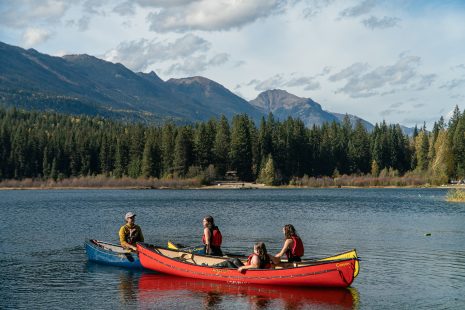 Image shows four people in two canoes on a lake surrounded by mountains.
