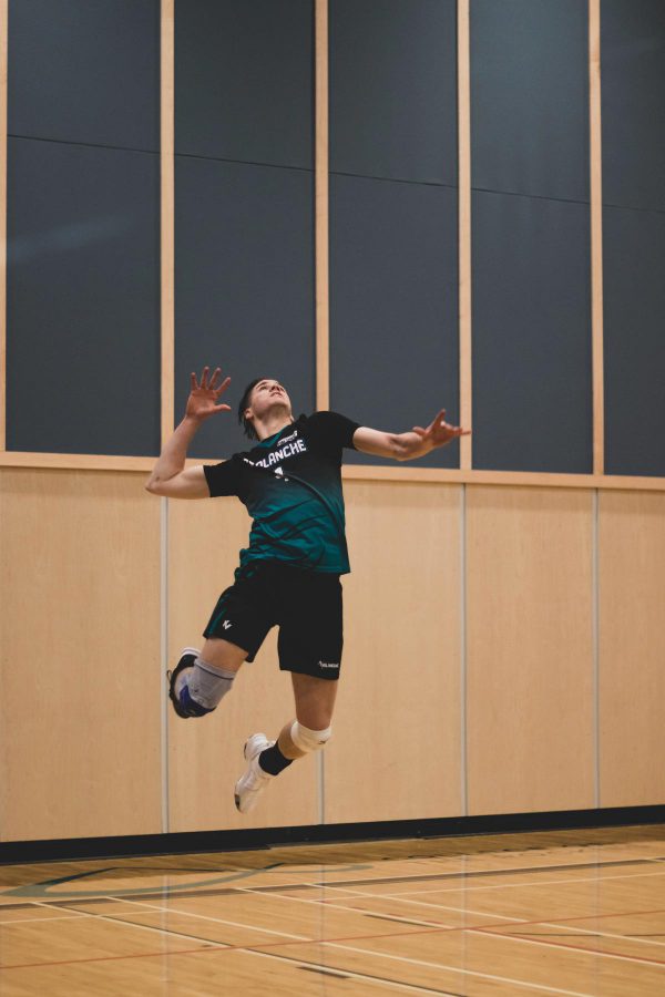 Image shows men's Avalanche volleyball team member jumping high in the air to spike ball.