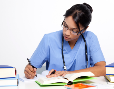 Image shows woman in scrubs with a stethoscope around her neck studying.