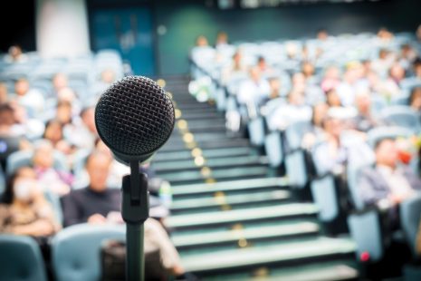 Image shows microphone set up with an audience in the background