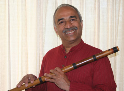 An image of musician Raj Rangayyan smiling at the camera, holding a bamboo flute.
