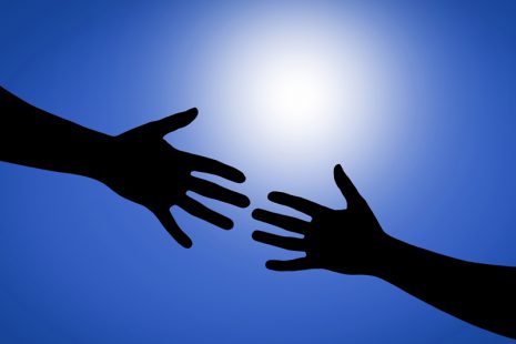 Image shows hands reaching toward each other with the sun shining behind them.