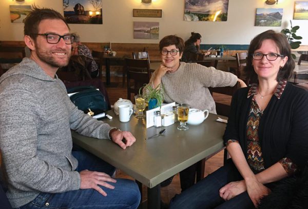 Image shows a man and two women sitting around a table at a coffee shop.