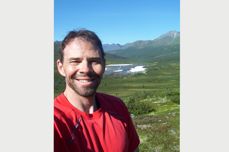 An image of a smiling man with fields and mountains in the background.