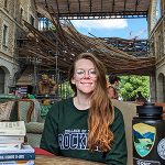 Image shows woman with long hair and glasses sitting outdoors