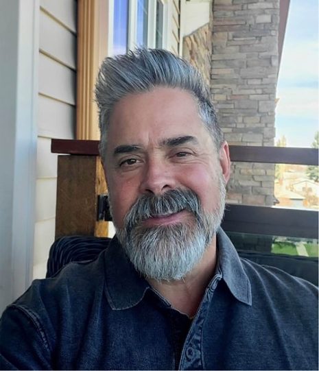 Image shows man with salt & pepper hair and goatee smiling at the camera