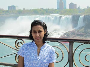 Image of a woman standing facing camera with a railing and waterfall behind her.