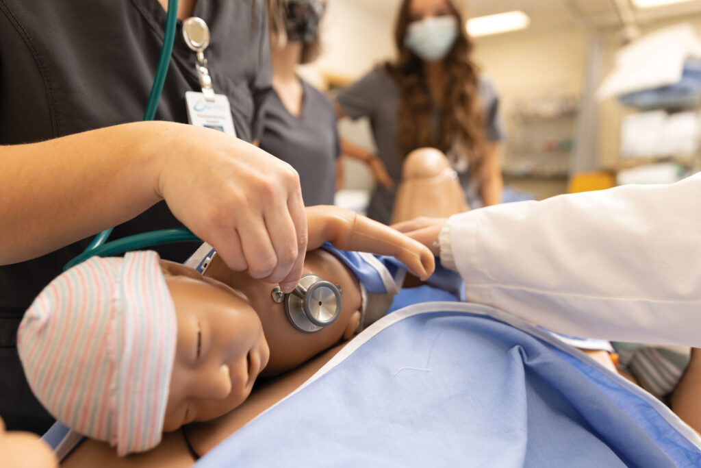 Image shows nursing students listening to heartbeat of baby manikin.