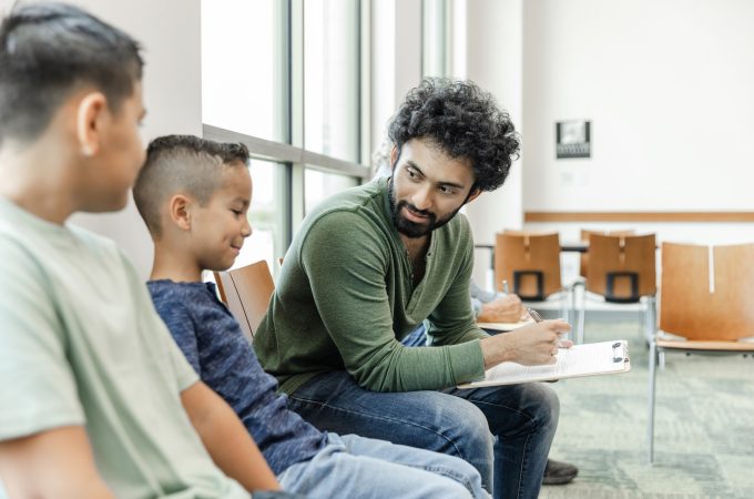 At the doctor's office, the young adult dad asks his elementary age son about his symptoms.