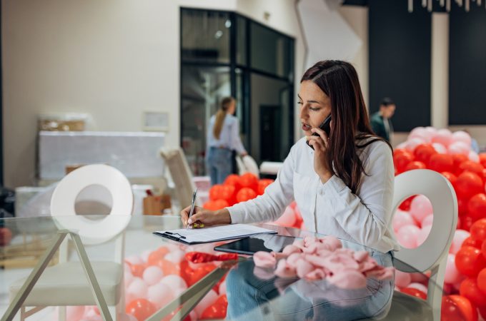 A female event planner sits in a restaurant and talks to new clients on the phone, writes down the details of the reservation and the decoration that the client wants