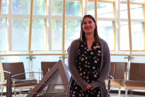 Woman in a flowered dress and grey sweater smiling at the camera