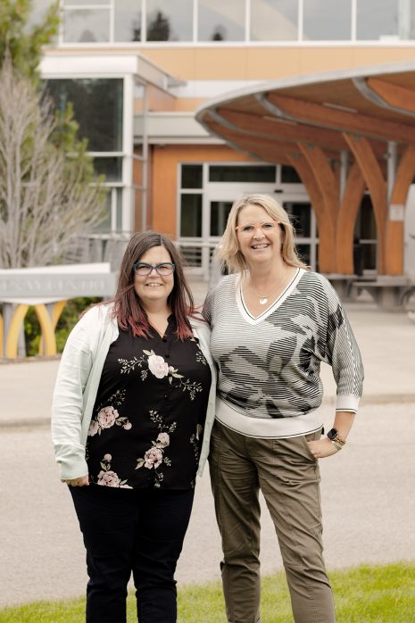 Image shows two women standing next to each other outside with College of the Rockies' main campus entrance showing behind them.