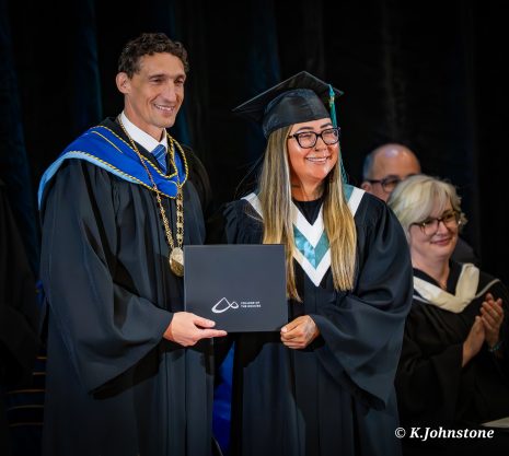 Image show smiling woman receiving her diploma at a graduation ceremony.