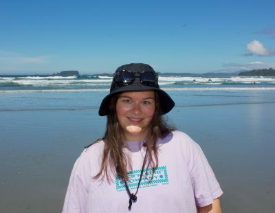 Image shows woman in a sun hat in front of a large body of water.
