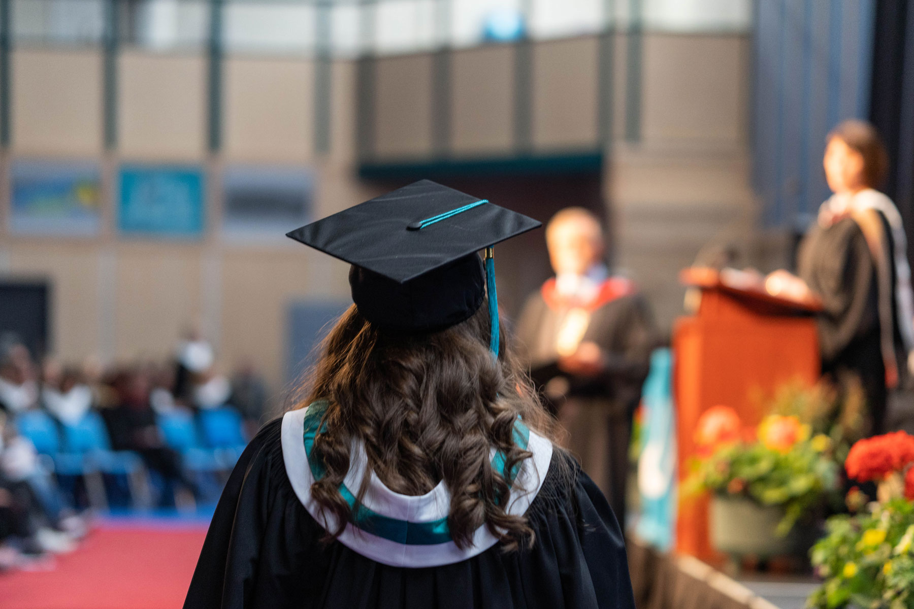 A graduate in cap and gown walking towards a stage.