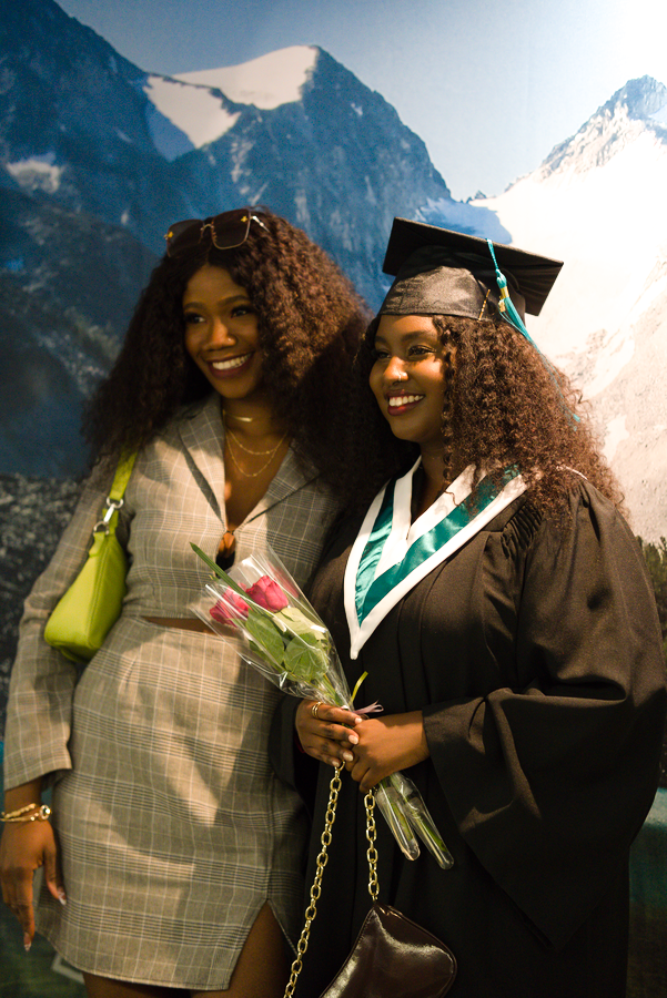 A female student in cap and gown with attendee at Graduation ceremony.
