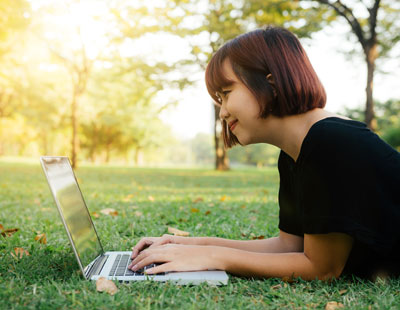 An image of a student laying on the grass using a laptop computer.