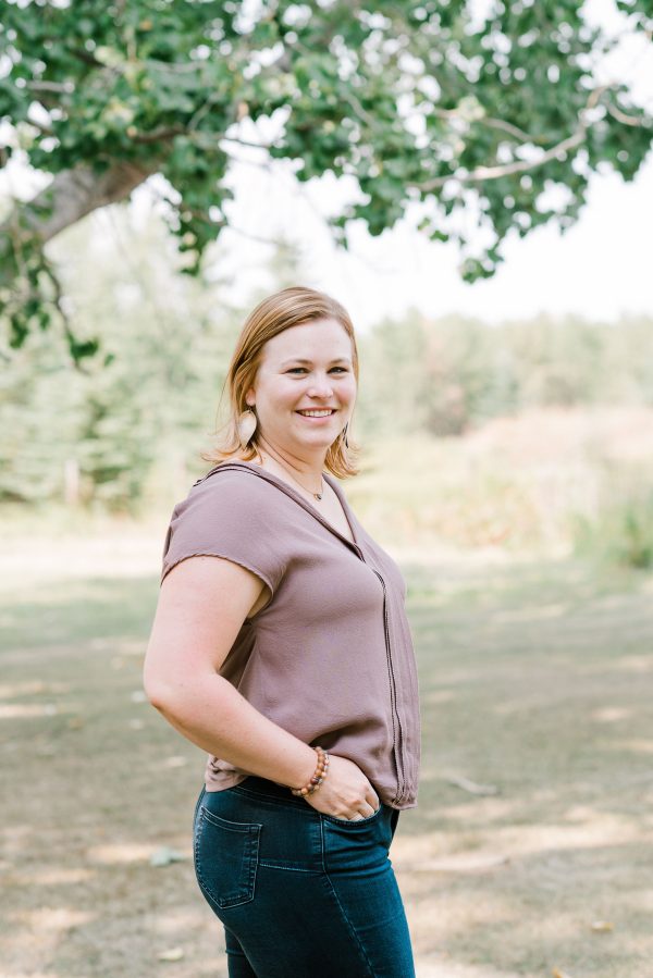 Image show smiling woman standing outdoors under a tree.